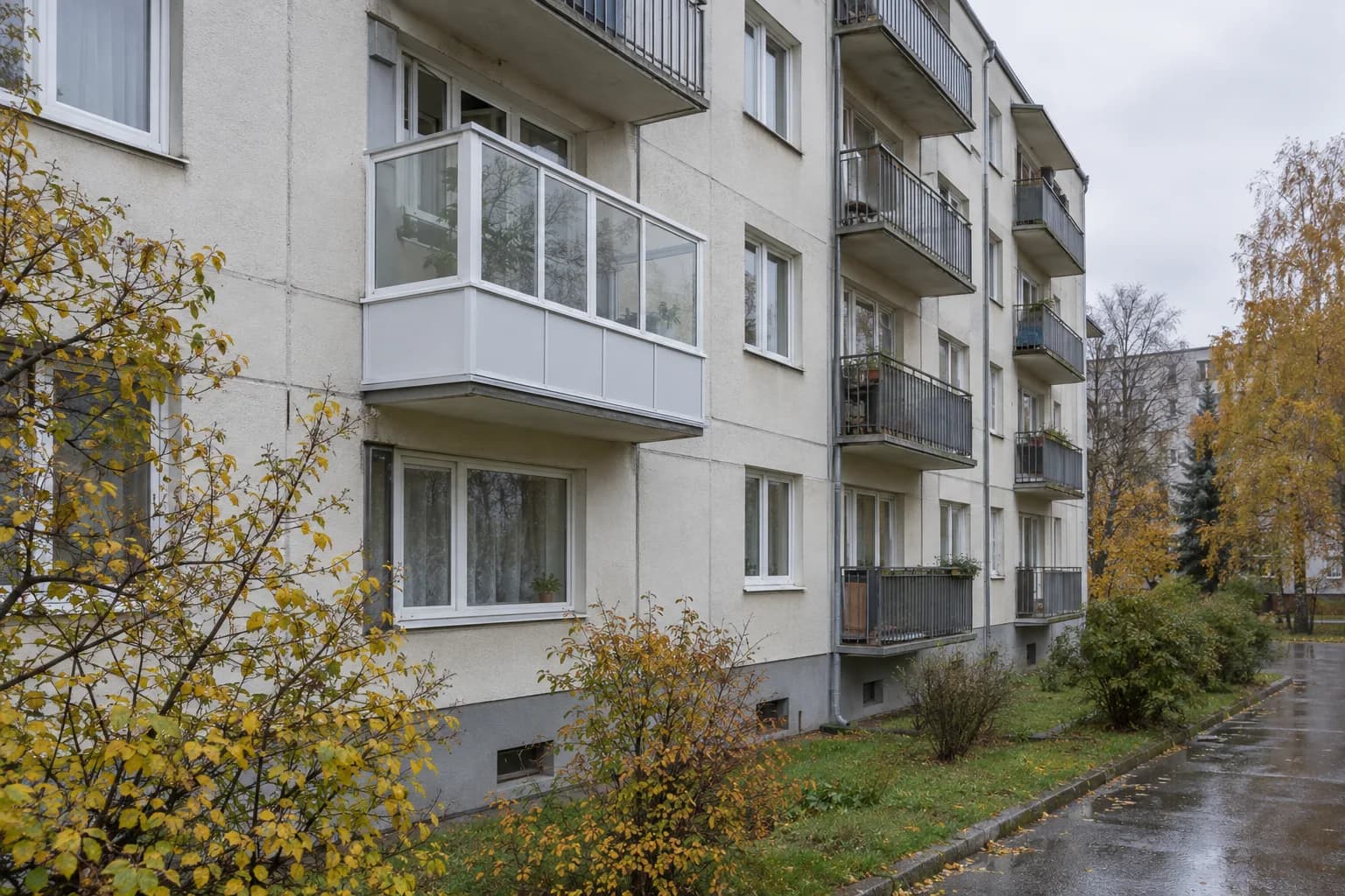 Daugiabučio fasadas: vienas balkonas įstiklintas baltais slankiojančiais stiklo skydais, gretimi balkonai dar atviri